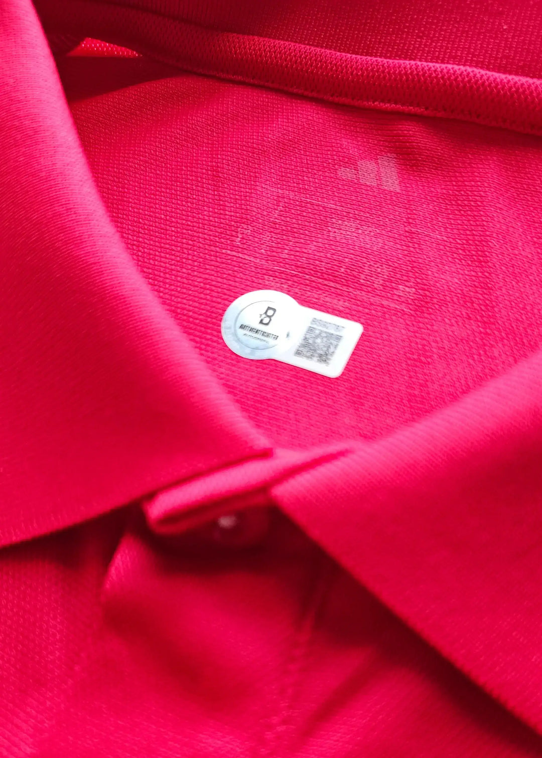 Inside view showing authenticity label with QR code on a red football shirt.