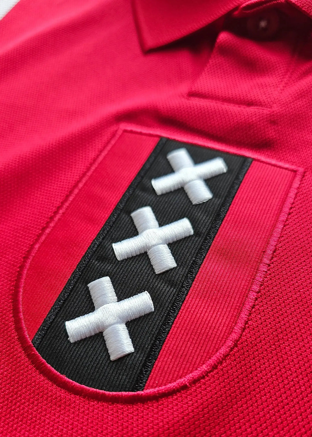 Crest detail featuring three white crosses on a black background within a red shirt.