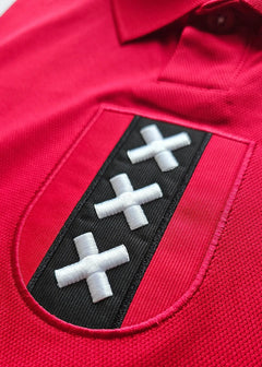 Crest detail featuring three white crosses on a black background within a red shirt.