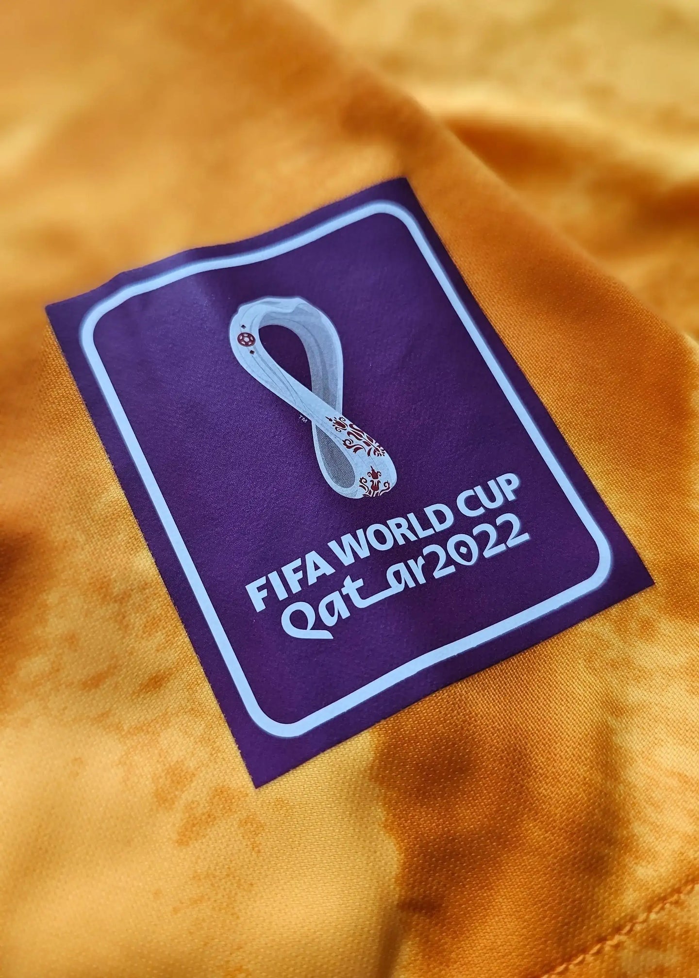 Detail view of FIFA World Cup Qatar 2022 patch on orange football shirt.