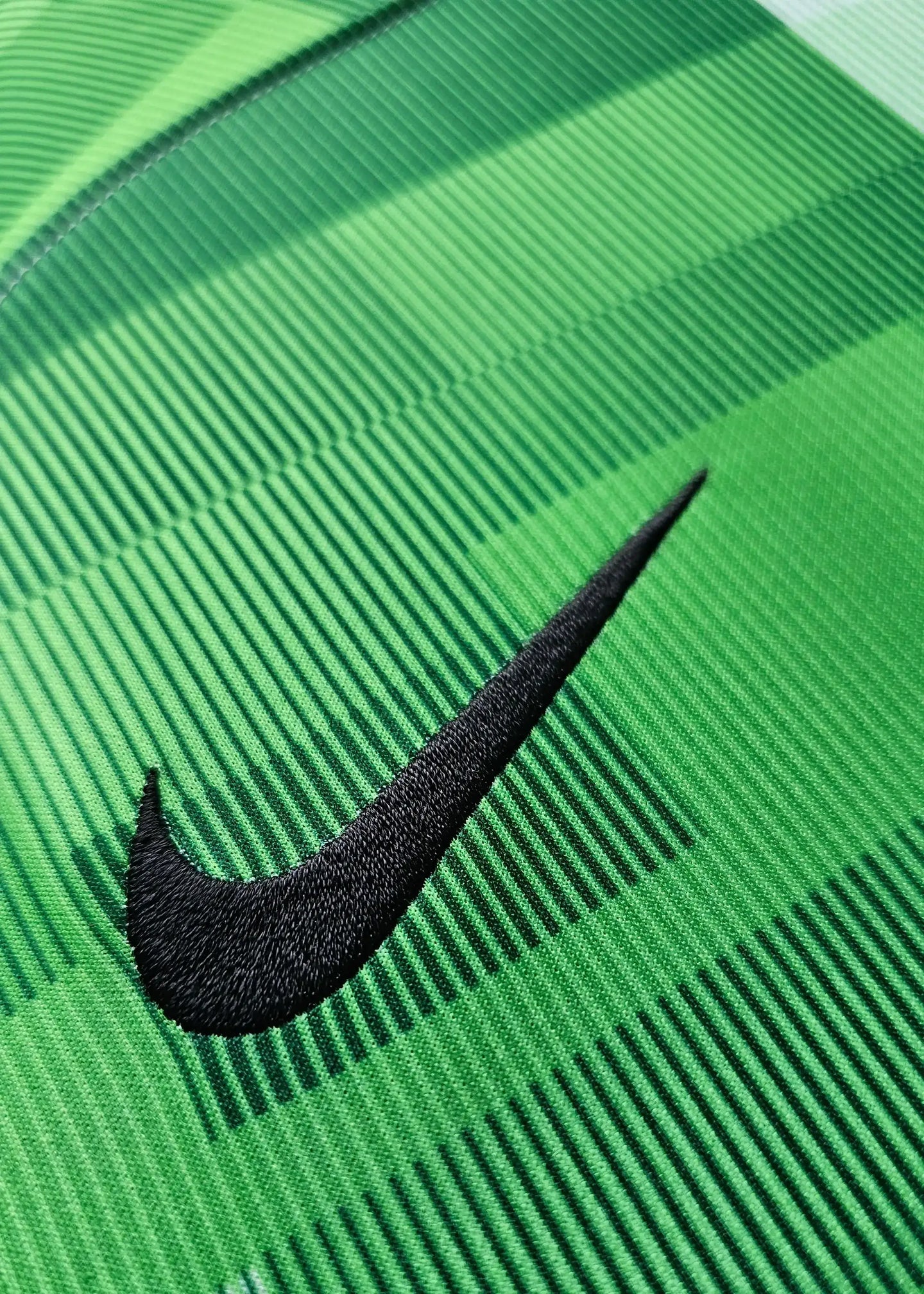 Close-up of the black Nike logo on a green football shirt with striped texture.