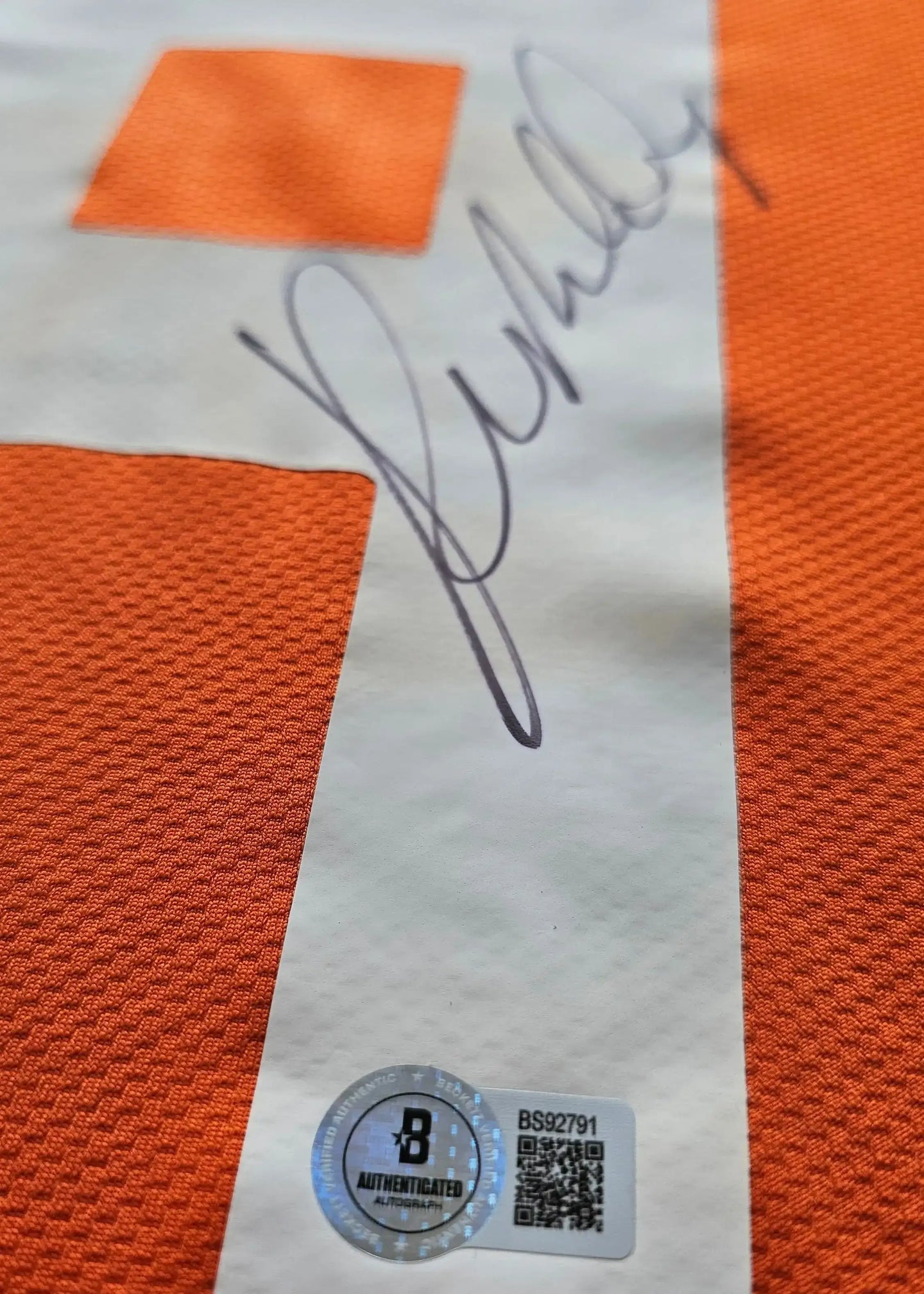 Close-up of the signature on an orange football shirt with No. 7 visible and an authentication sticker.