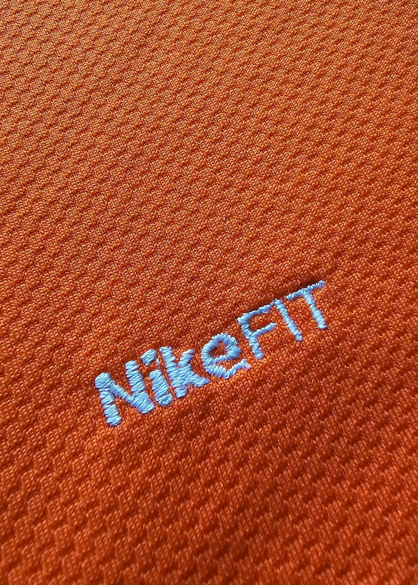 Close-up detail showing NikeFIT logo embroidered in blue on orange fabric.