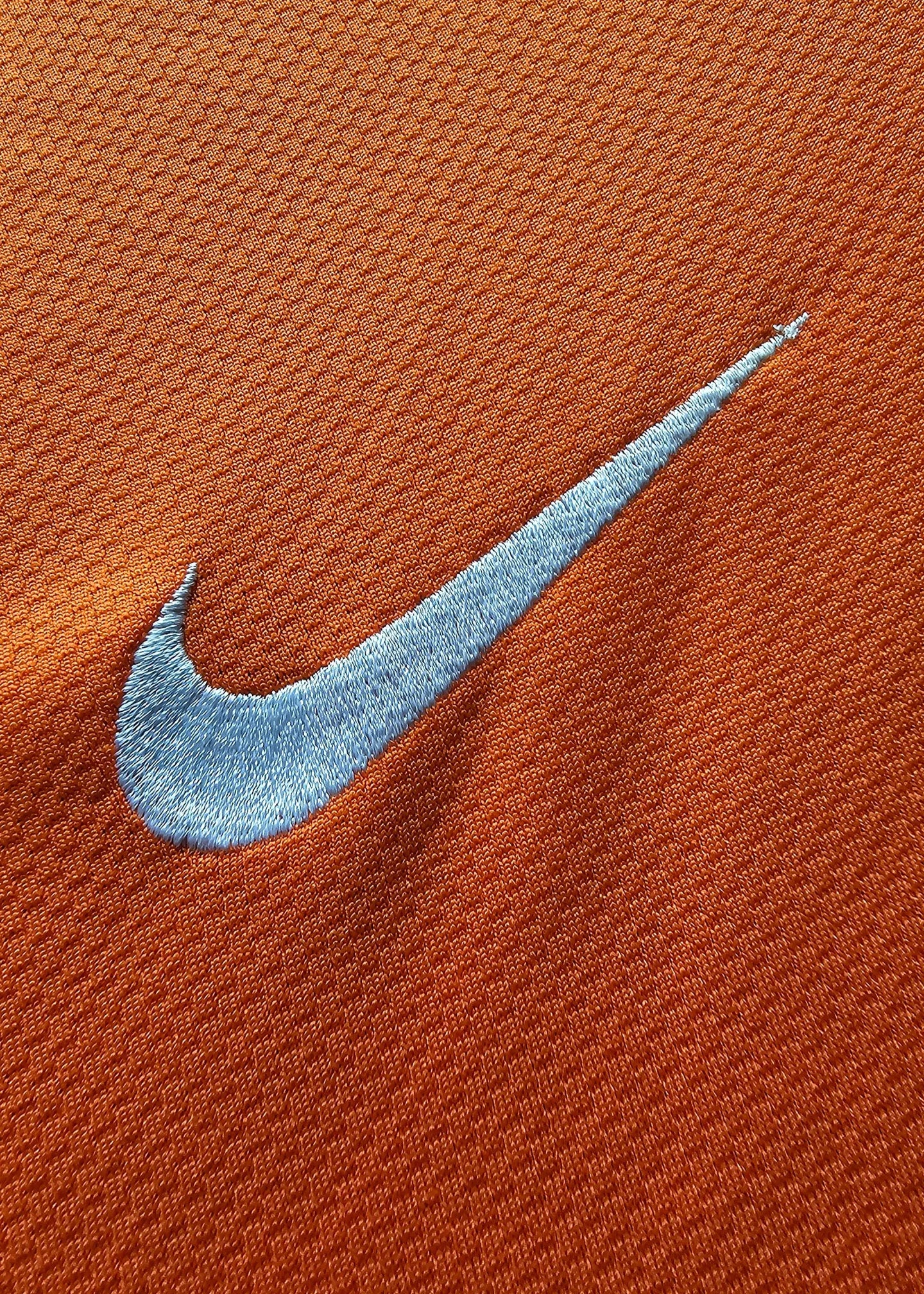 Close-up detail of the Nike logo embroidered in blue on an orange football shirt.