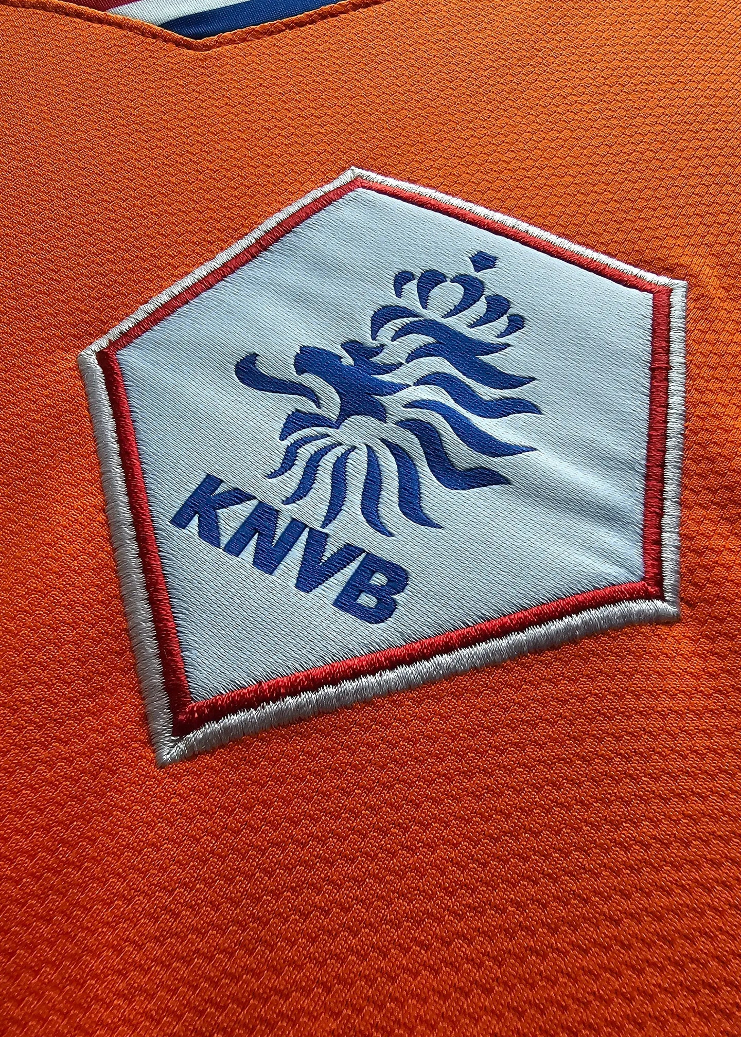 Close-up of the KNVB crest on an orange football shirt, featuring a blue lion and 'KNVB' text.
