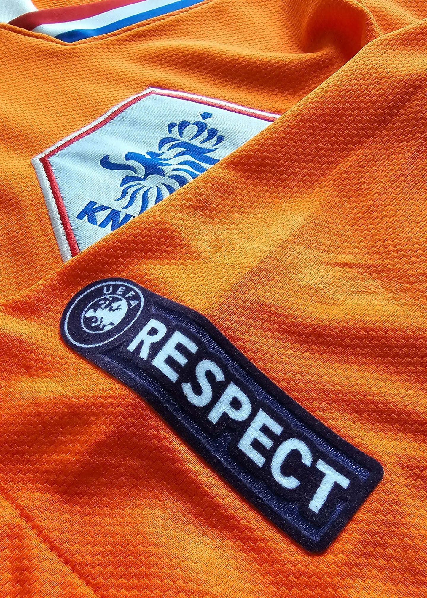 Close-up showing the KNVB crest and UEFA RESPECT badge on an orange football shirt.