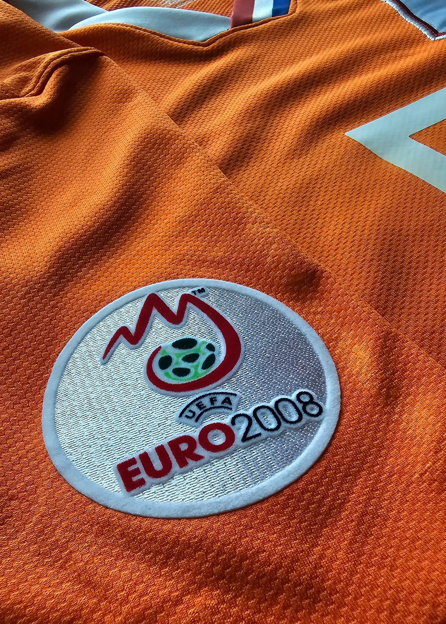 Crest detail featuring UEFA EURO 2008 logo on an orange football shirt.