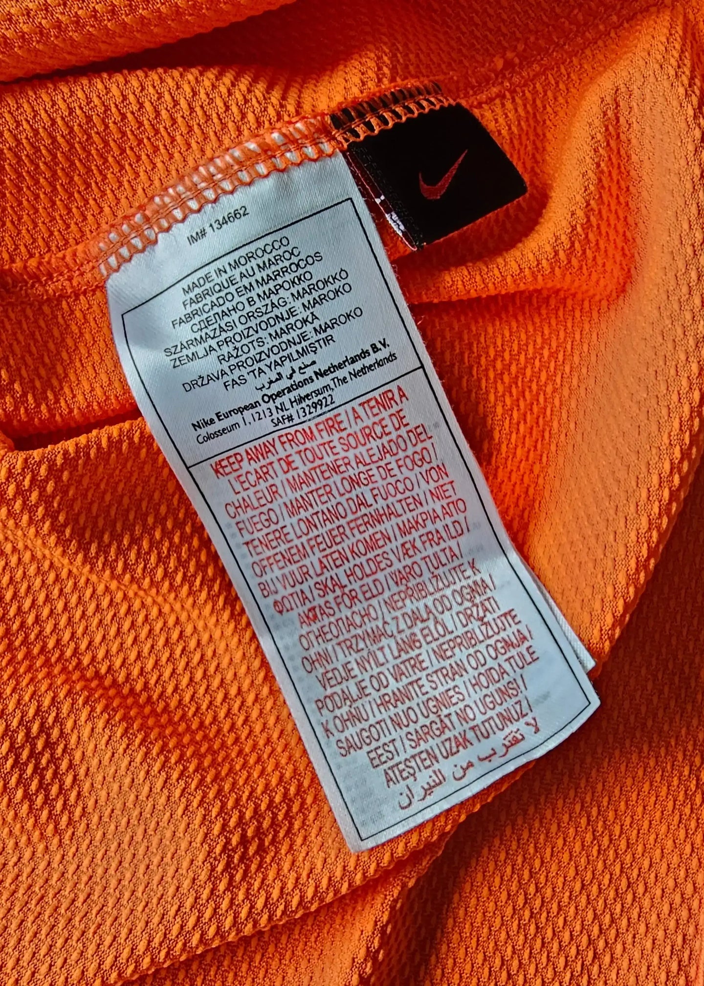 Nike tag with care instructions and origin details on an orange football shirt.