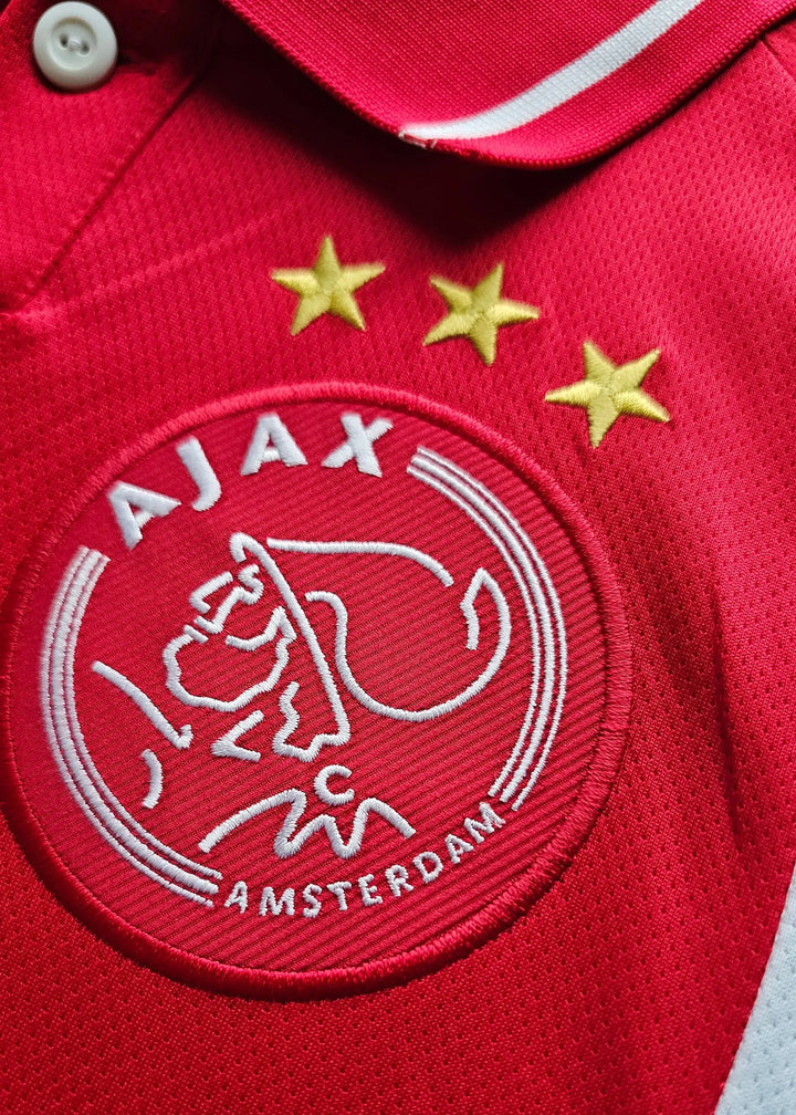 Close-up of Ajax crest with three stars and 'AJAX AMSTERDAM' text.