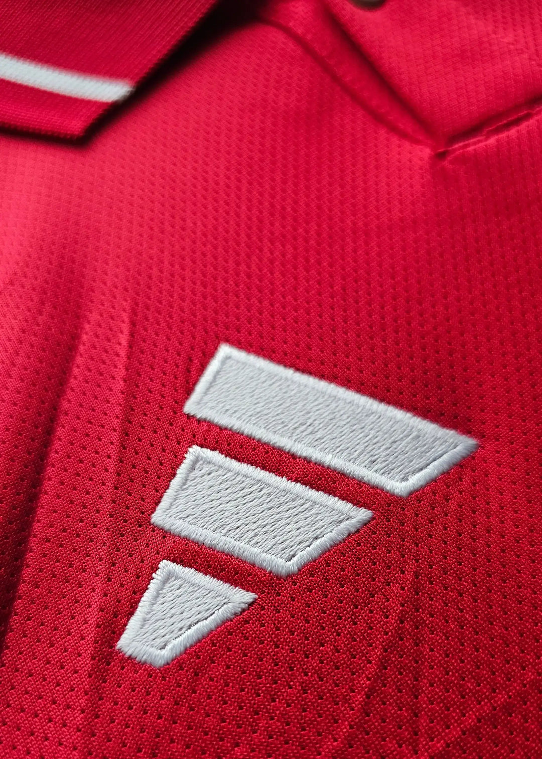 Close-up detail of red fabric with white stripes and logo on football shirt.
