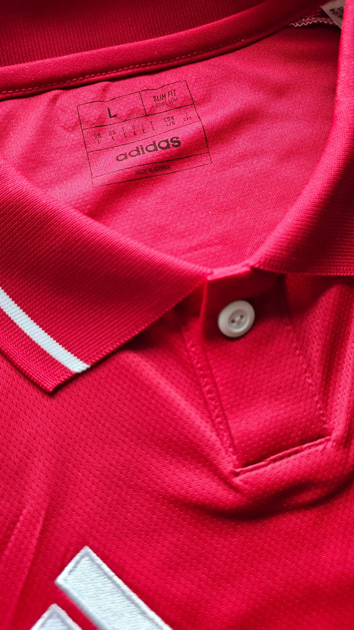 Close-up of the buttoned collar on Brian Brobbey's red Ajax shirt, showing the adidas size and care label (L, Slim Fit) and white adidas stripes at the hem.