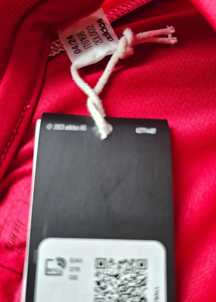 Care label attached to the red football shirt showing adidas branding and size details.