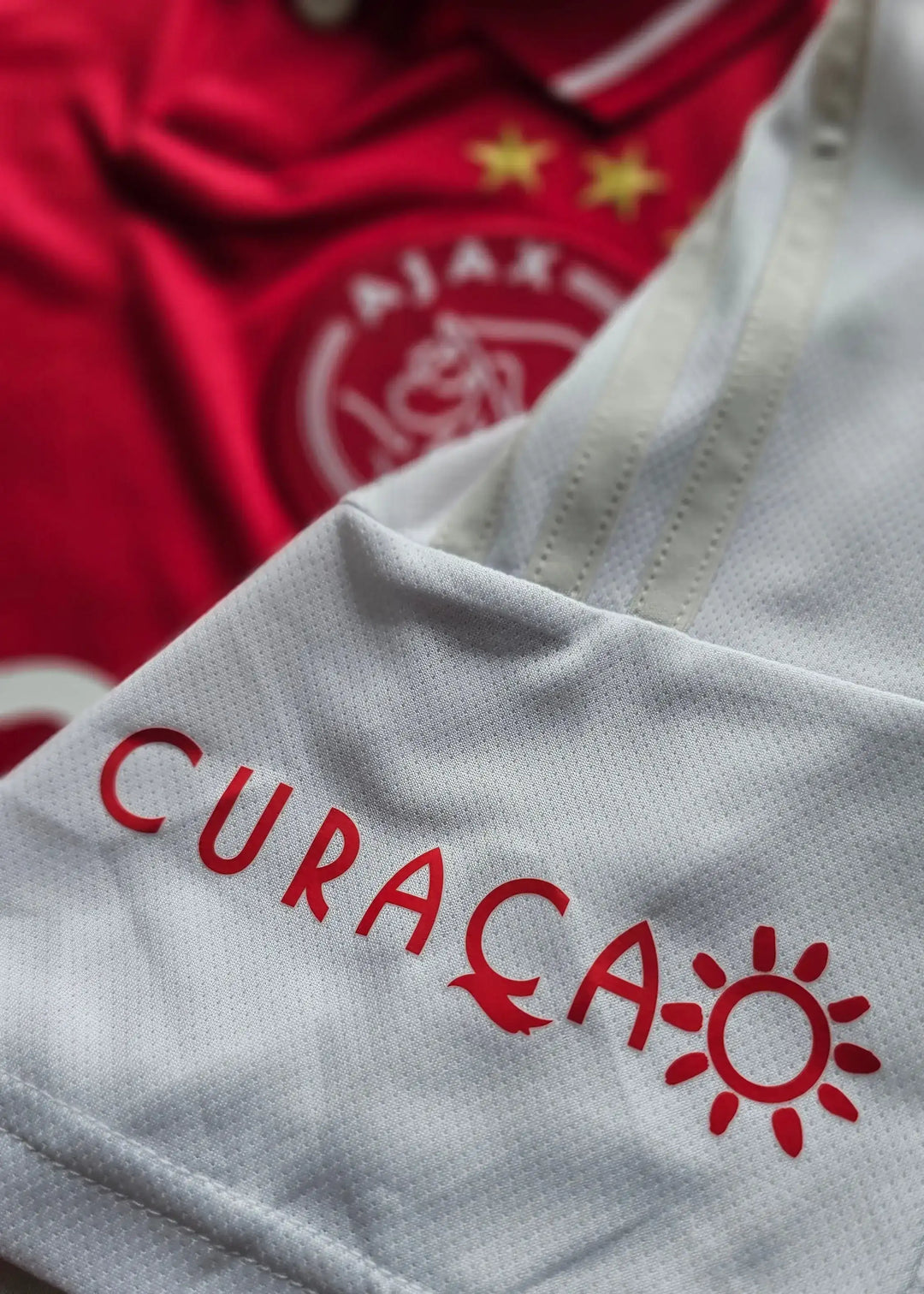 Front view showing Ajax crest with two stars and CURAÇAO printed in red on white fabric.