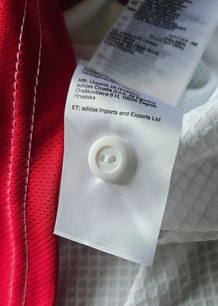 Detail view showing a white tag with care instructions and button on a red football shirt.