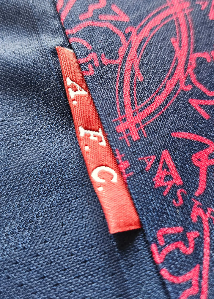 Close-up of the small red 'A.F.C.' tag on the navy fabric of Jari Litmanen's 1994-95 Ajax away shirt, printed with a red swirling pattern.