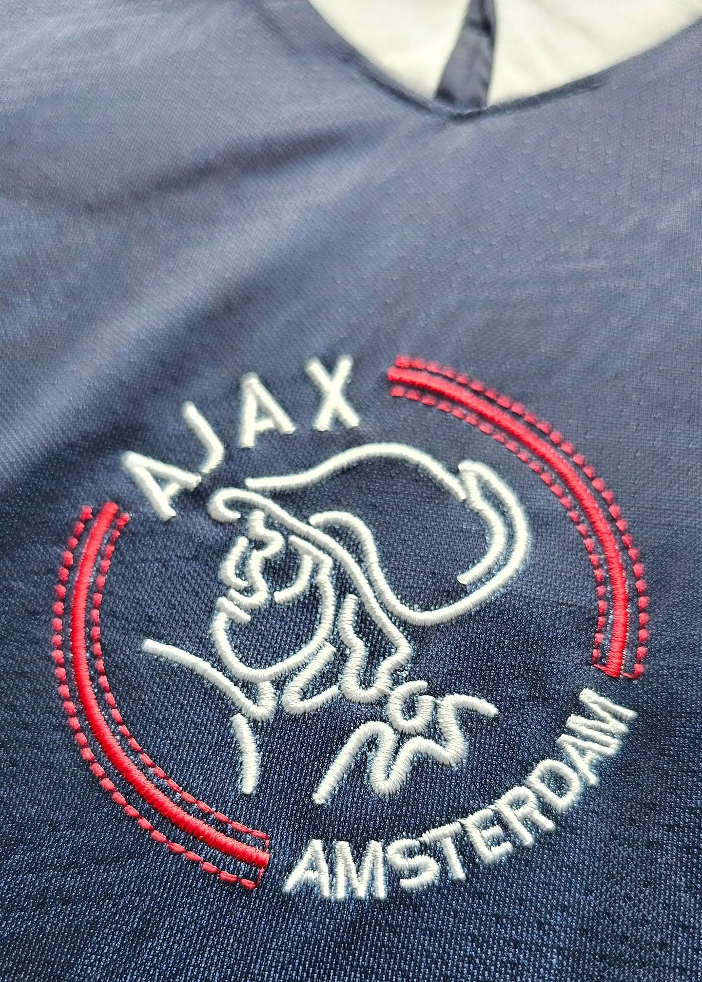 Close-up of Ajax crest featuring silhouette and AMSTERDAM text in red and white embroidery.