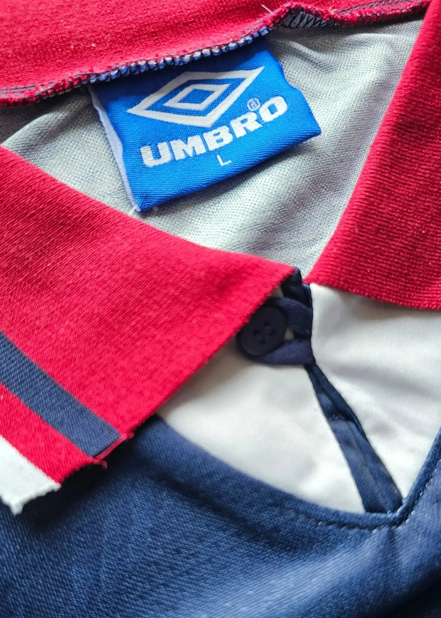 Close-up of collar featuring Umbro label in blue and red with button detail.
