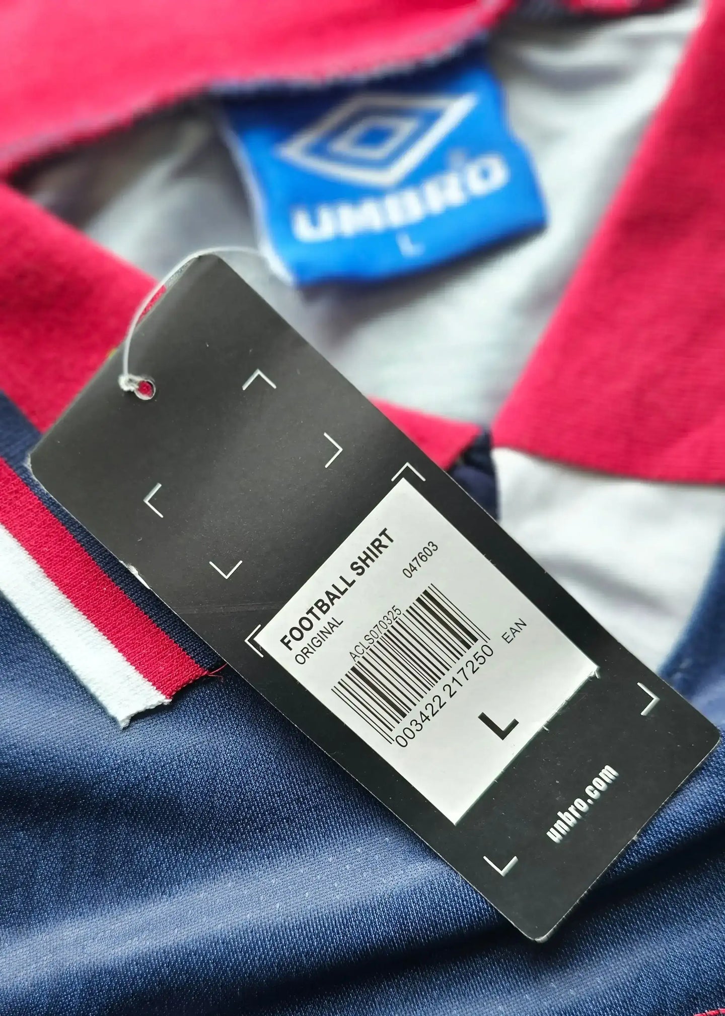 Tag detail showing size L, original label, and Umbro logo on a navy football shirt.