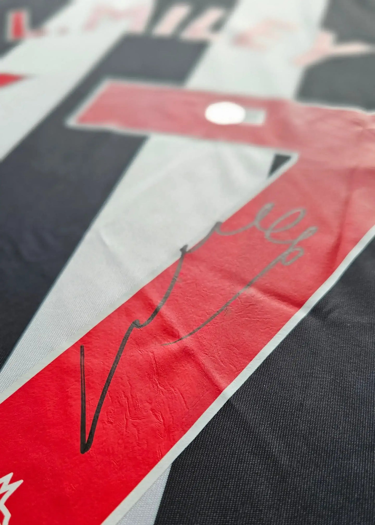 Close-up view of signature detail on the Lewis Miley signed football shirt, featuring design elements in black and red.
