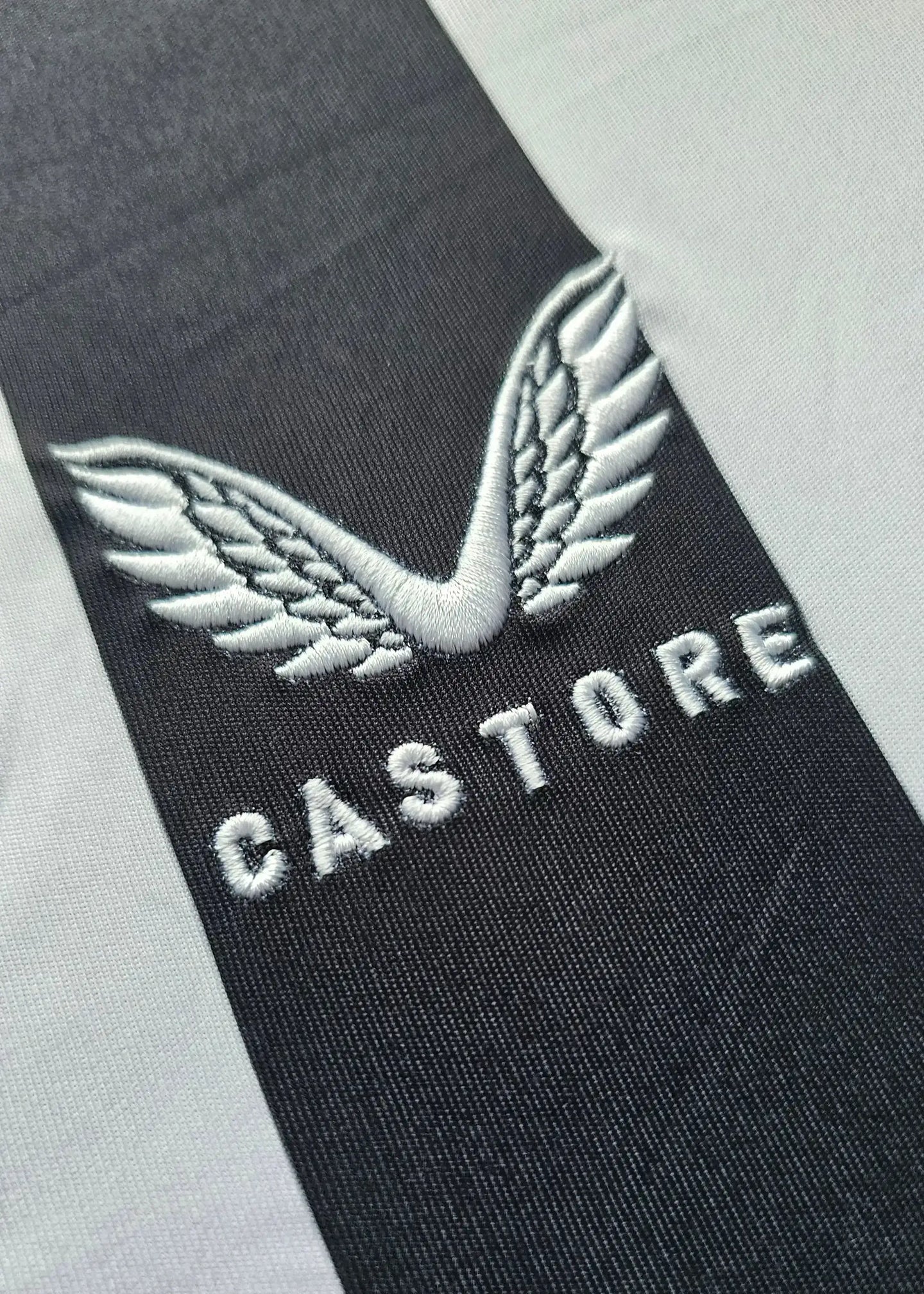 Close-up of the CASTORE logo featuring wings on a black and white striped football shirt.