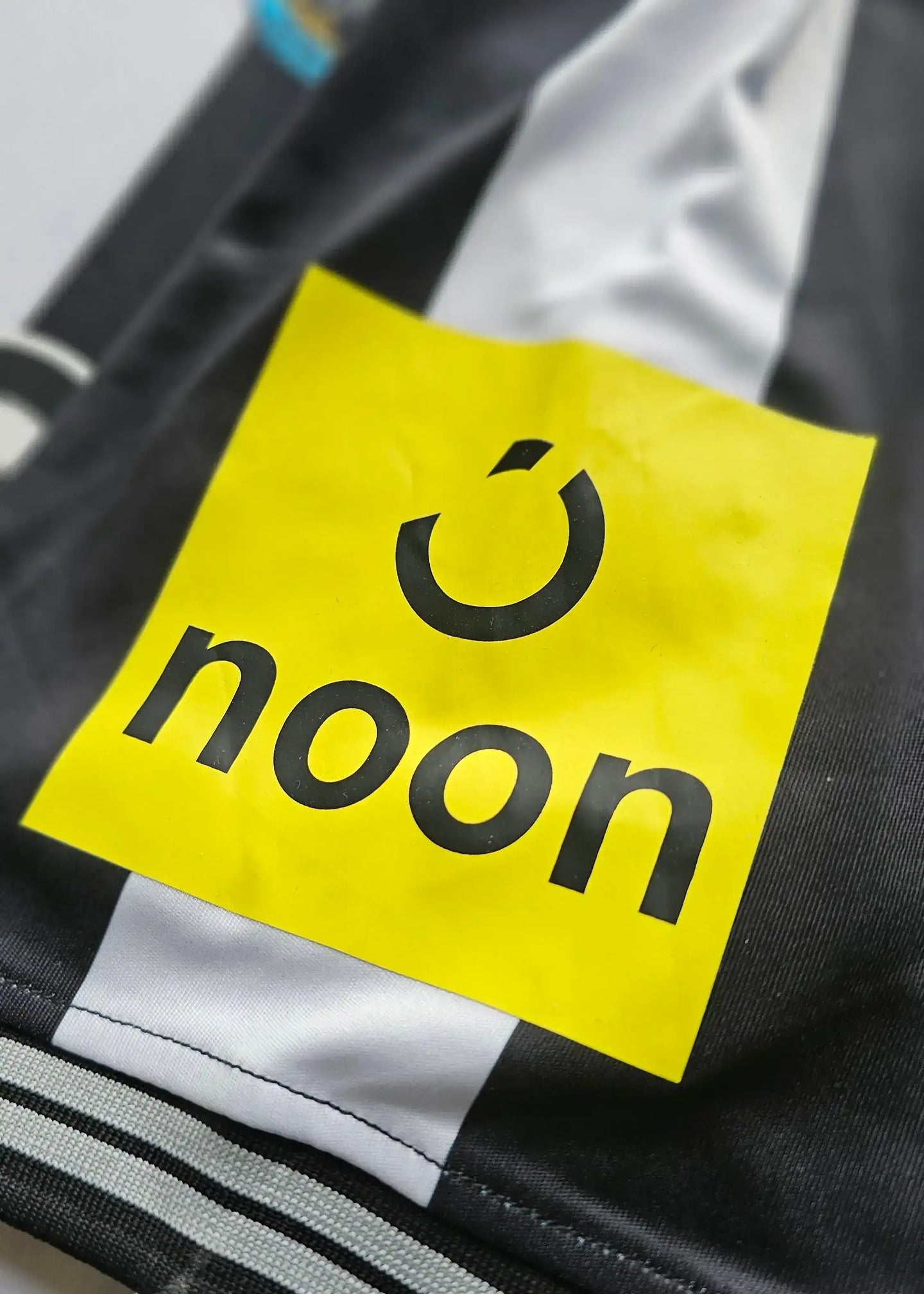 Close-up of the "noon" sponsor logo on the black and white striped football shirt.