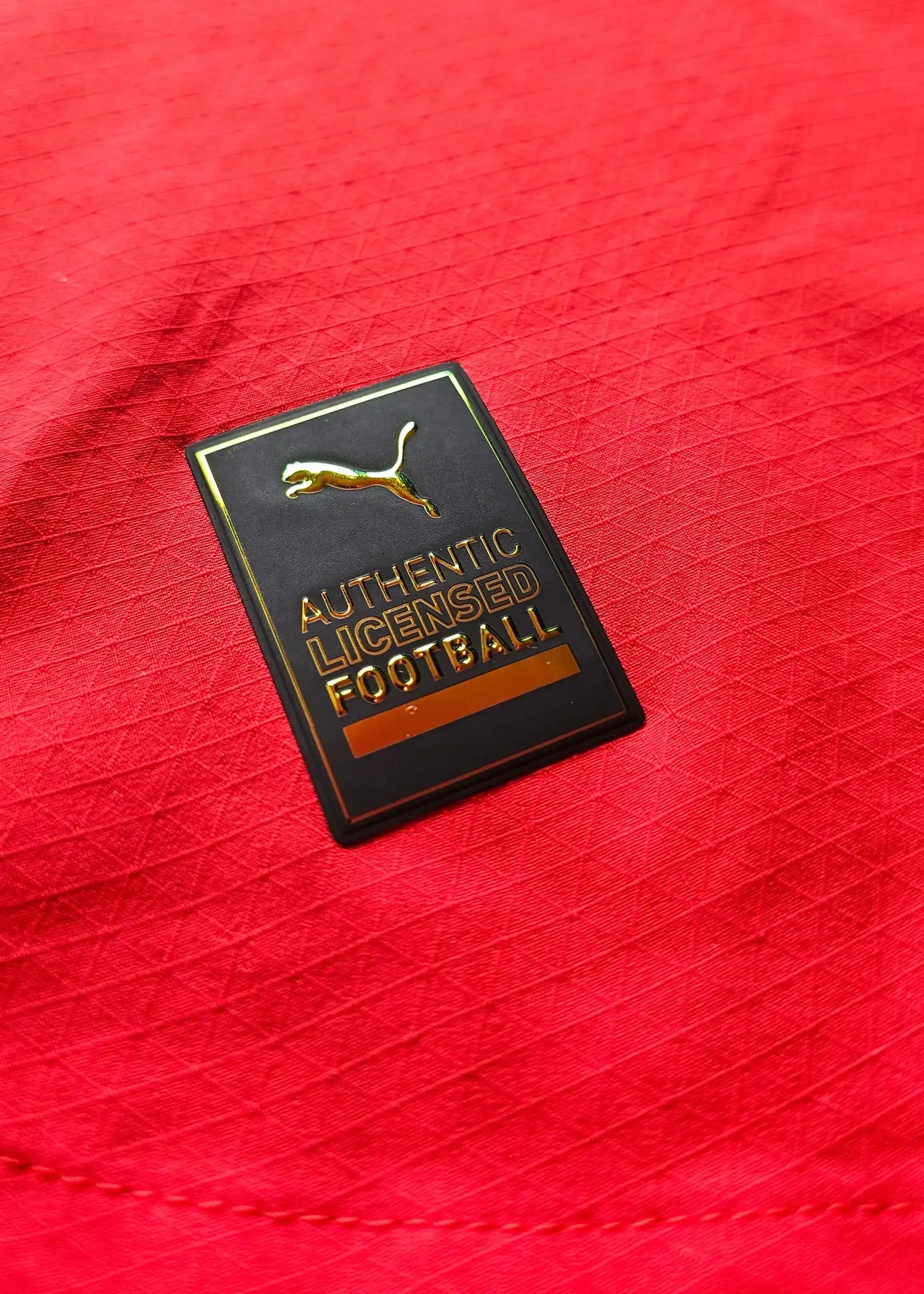 Puma tag featuring gold embossed text 'AUTHENTIC LICENSED FOOTBALL' on a red fabric background.