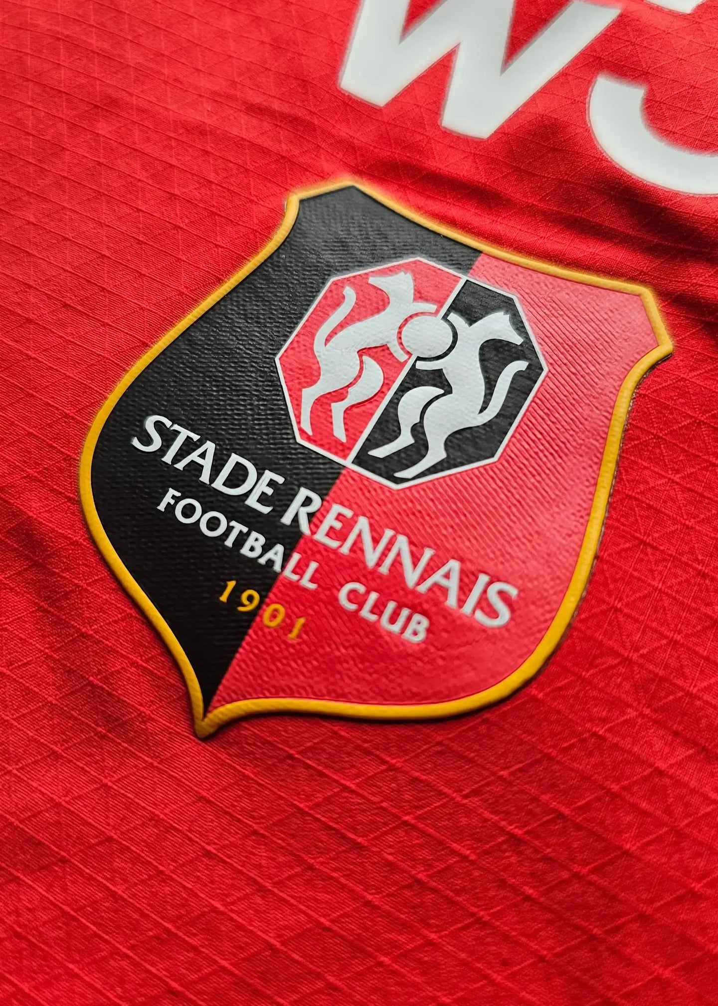 Detail of the Stade Rennais F.C. crest with 'STADE RENNAIS FOOTBALL CLUB' and '1901' on a red shirt.