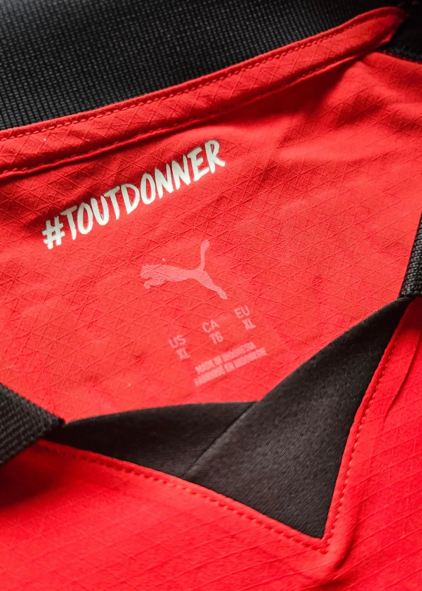 Red jersey collar with Puma logo and #TOUTDONNER text, showing care label details.