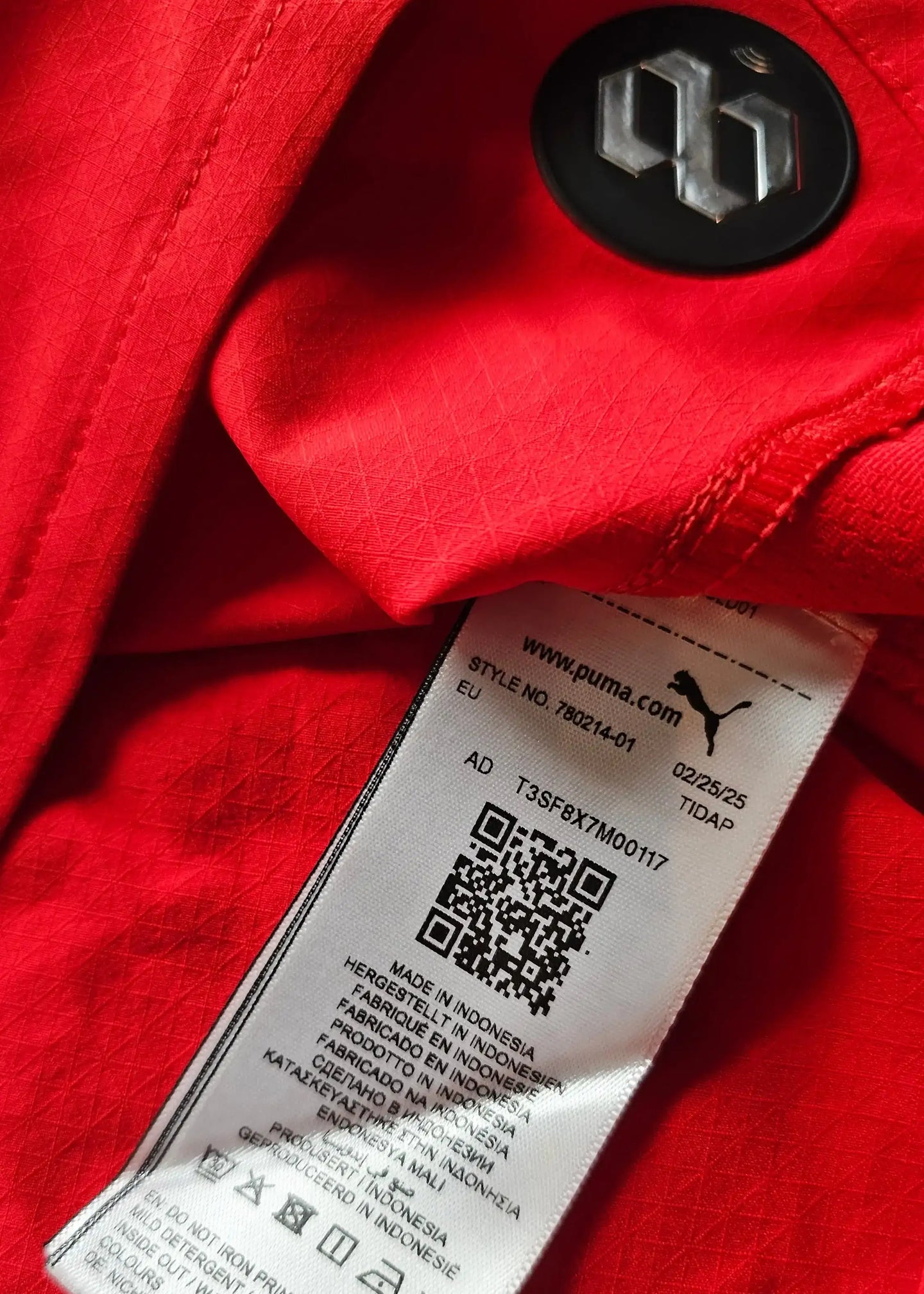 Red football shirt with Puma branding and label details, including QR code and care instructions.
