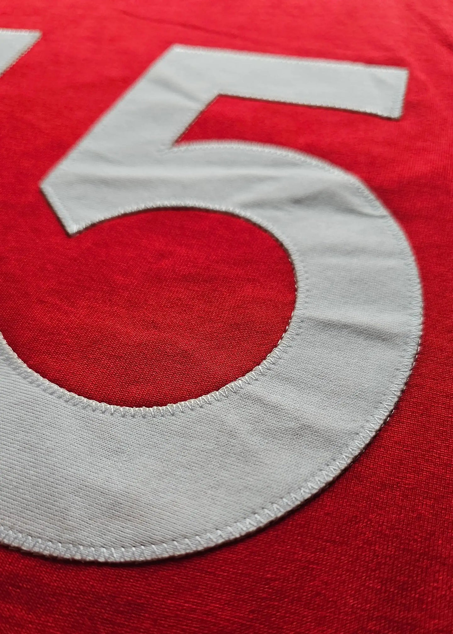 Close-up of the number 15 in white stitching on a red Ajax jersey.