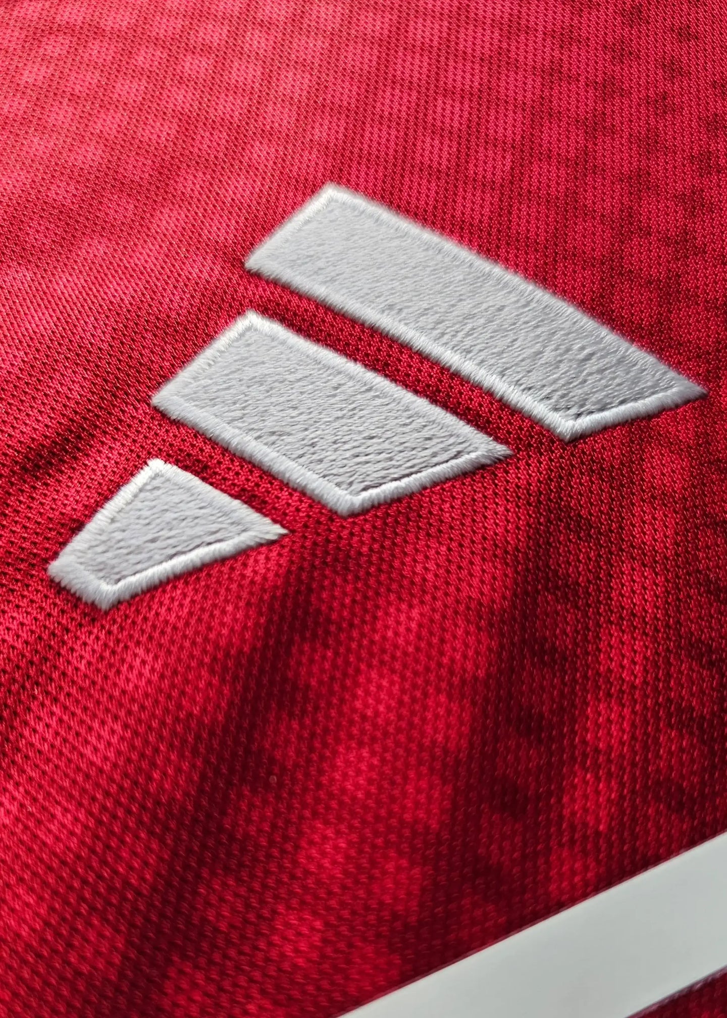 Close-up of the white adidas logo on a red football shirt.