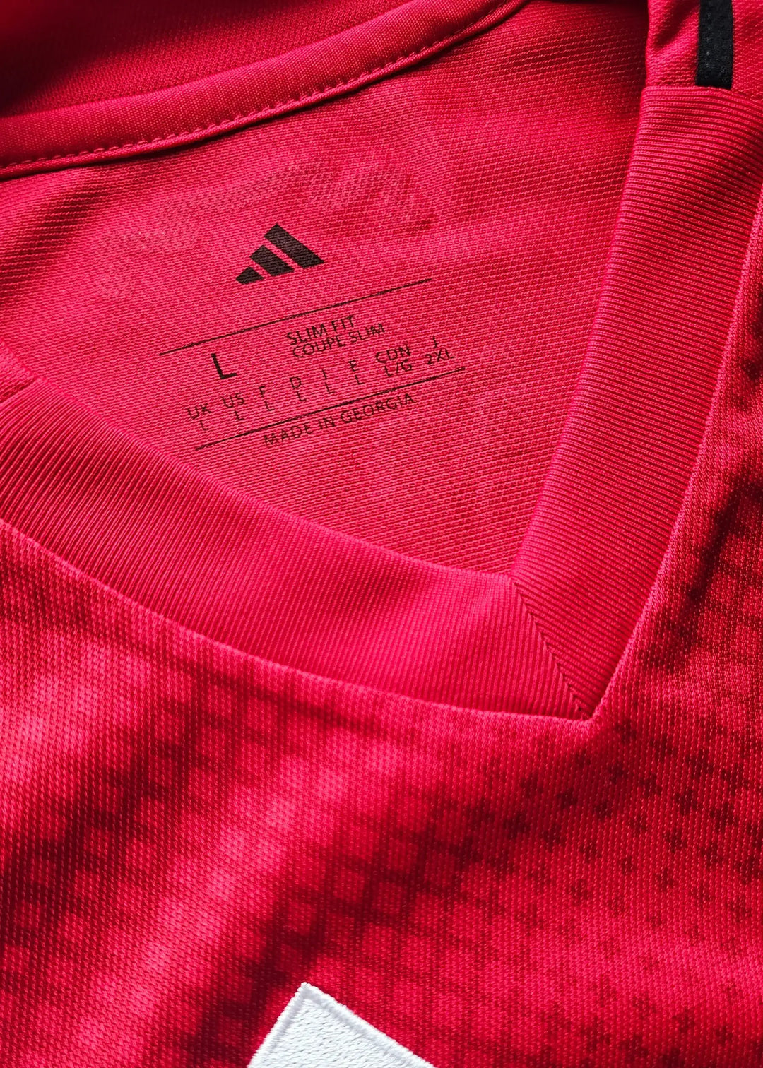 Size L tag with adidas logo and care instructions on a red football shirt.