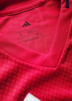 Size L tag with adidas logo and care instructions on a red football shirt.