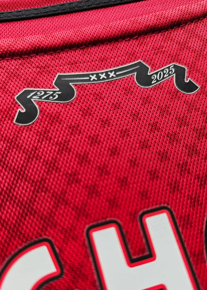 Close-up showing a red football shirt with black design elements featuring 1975, xxx, and 2025.