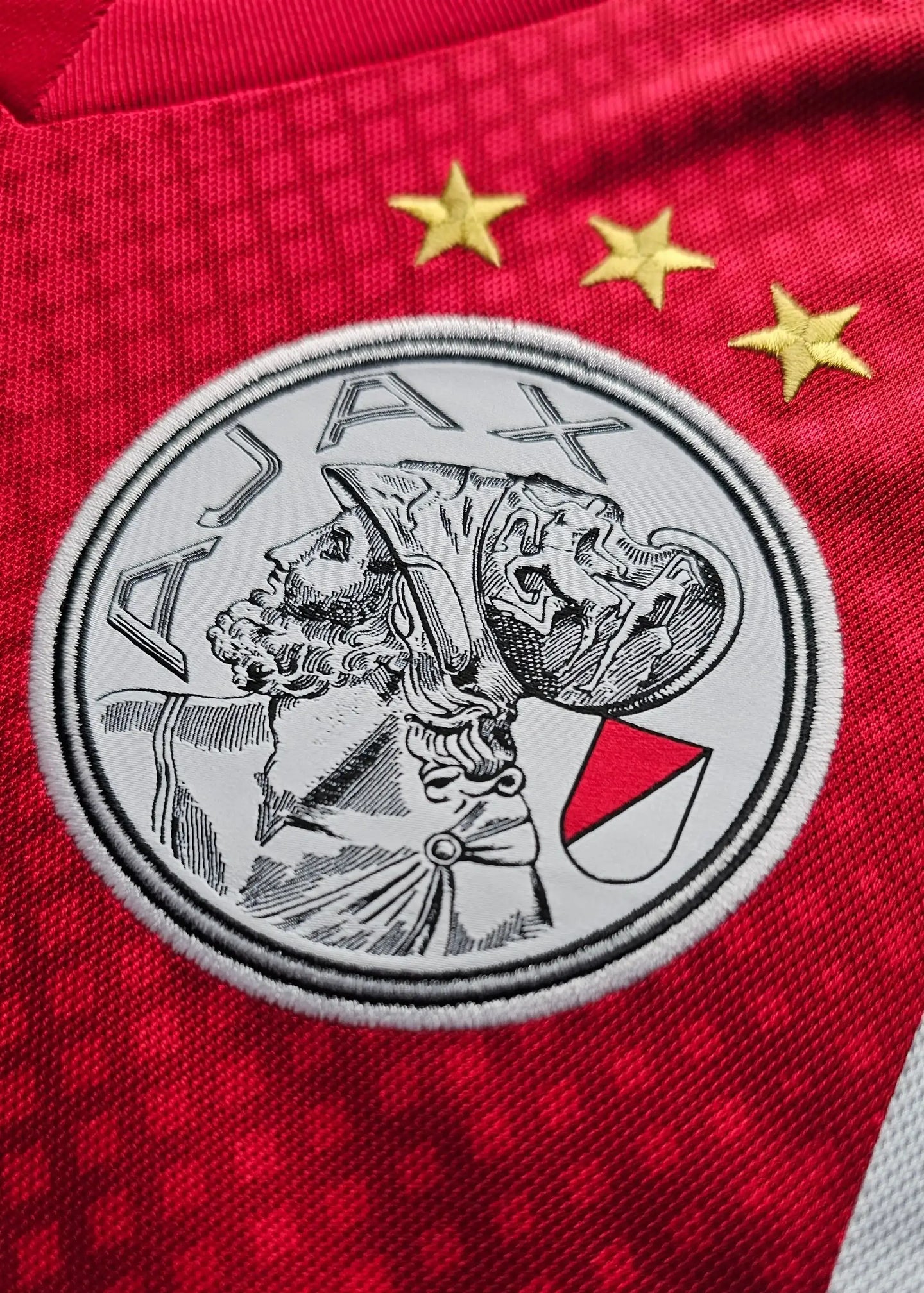 Close-up of AFC Ajax crest with three stars on a red background.