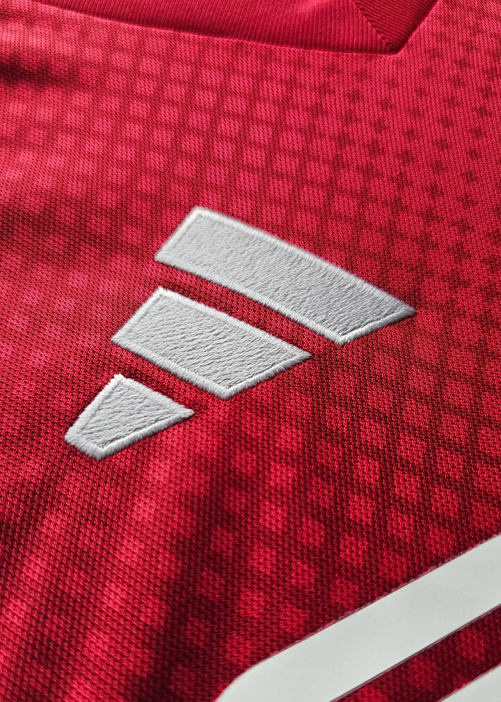 Close-up of the white adidas logo on a red football shirt's fabric with textured pattern.