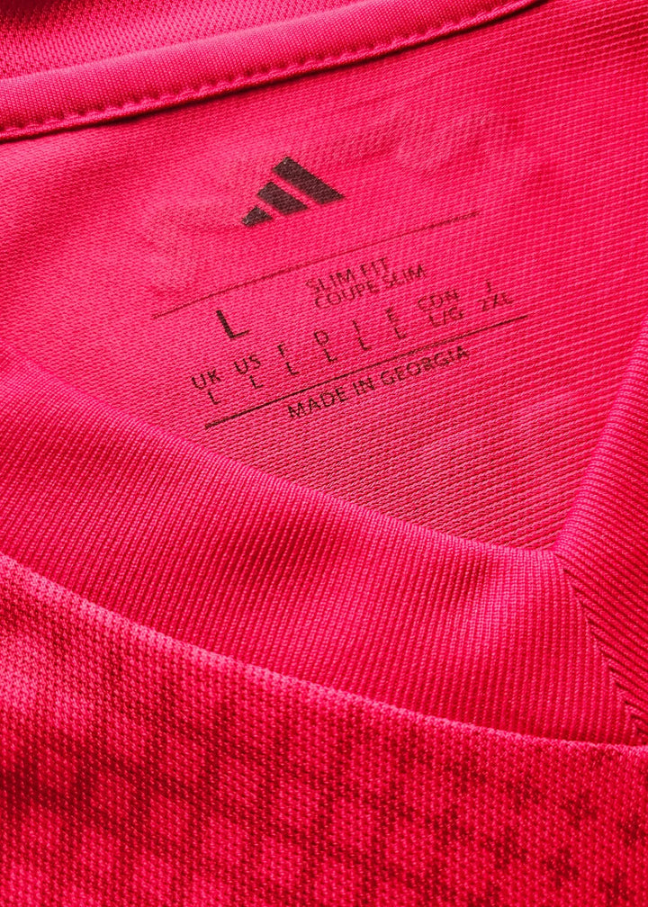 Care label showing size L, slim fit, and manufacturing details on a red adidas football shirt.