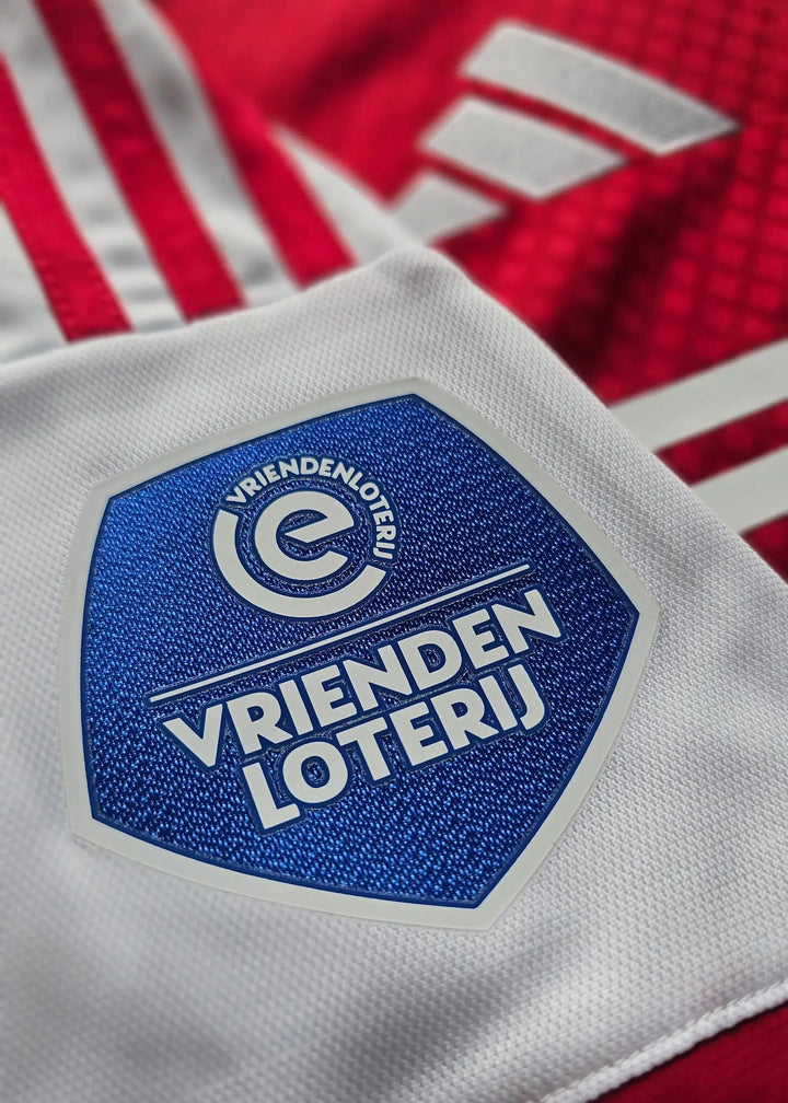 Close-up of the VRIENDENLOTERIJ logo on a red and white football shirt with three stripes.