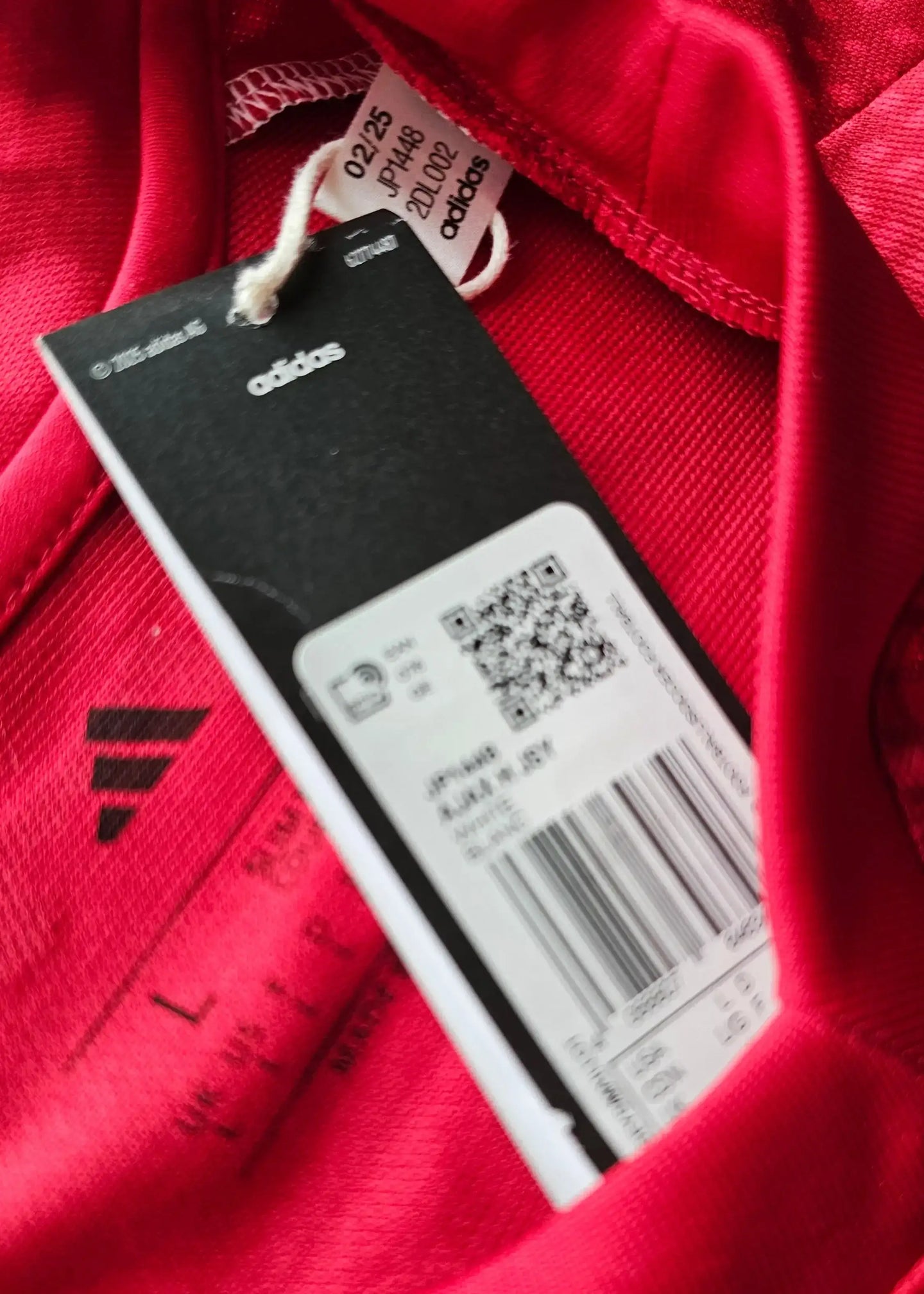 Detail view showing adidas tag, size L, and limited edition number 02/25 on a red football shirt.