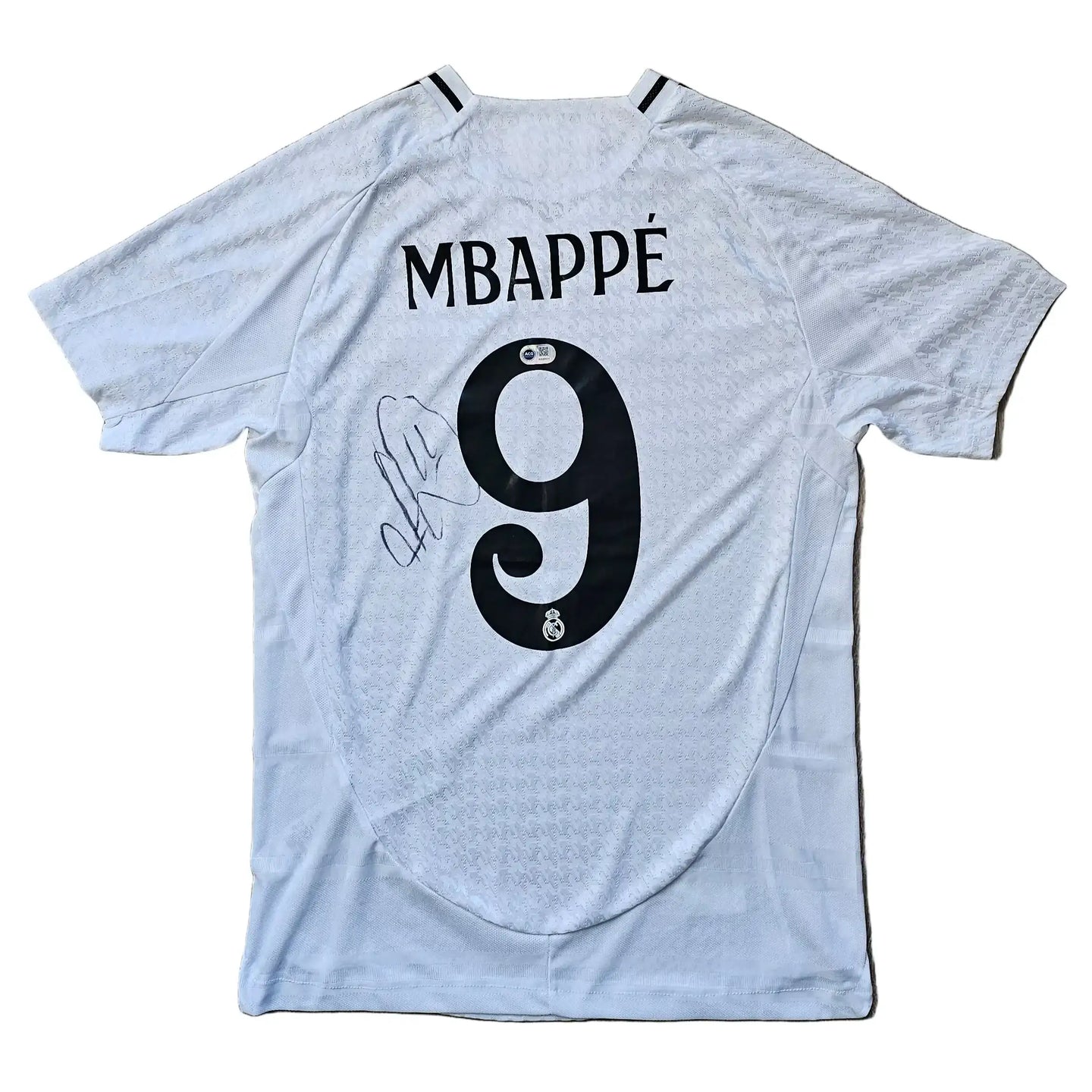 White football shirt with 'MBAPPÉ' and No. 9, featuring a visible signature and Real Madrid crest.