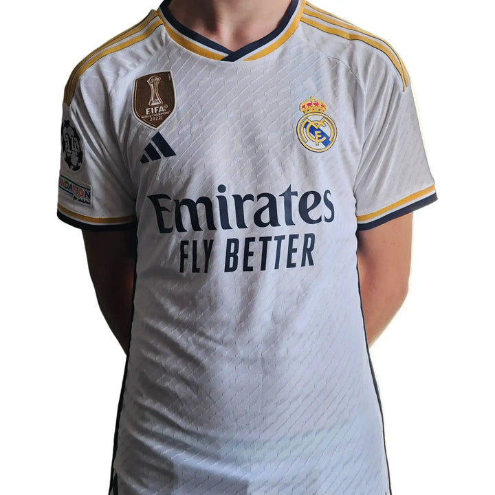 White Real Madrid shirt featuring Emirates sponsor text and crest, with Jude Bellingham&