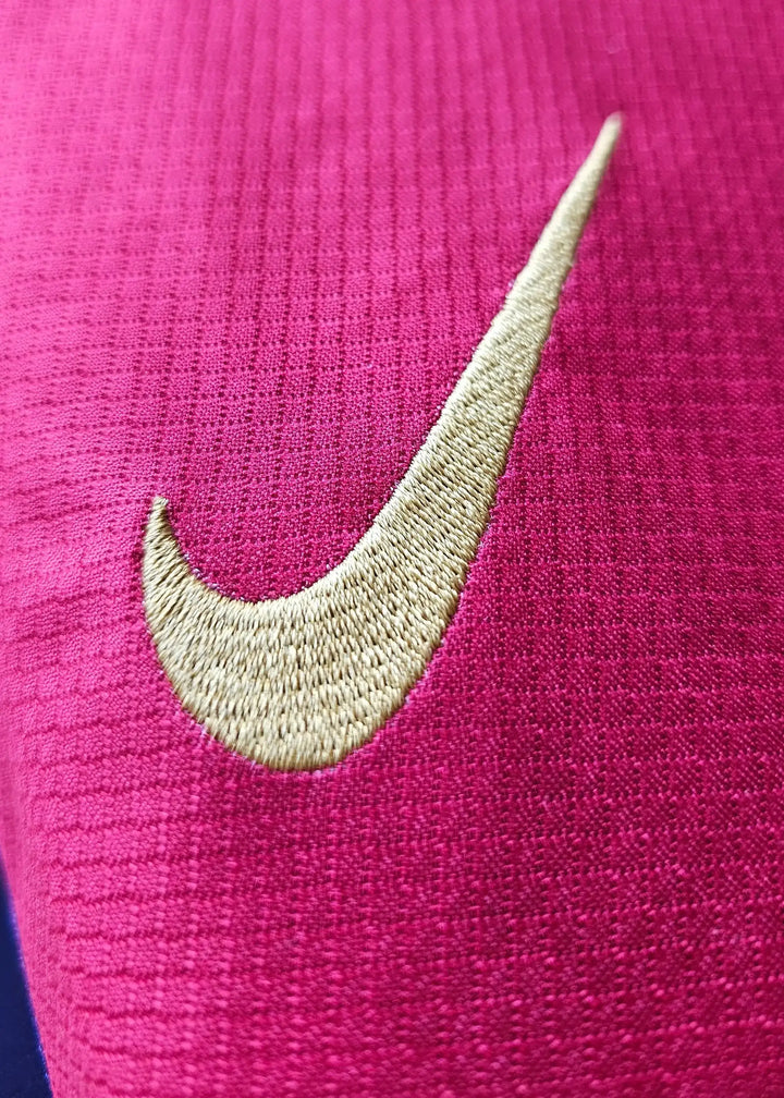 Close-up of the embroidered gold Nike swoosh on a pink FC Barcelona football shirt.