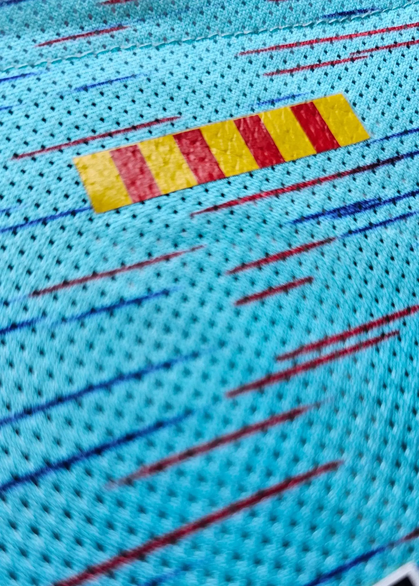 Close-up of the blue Barcelona 2023-2024 away shirt featuring red and yellow horizontal stripes.
