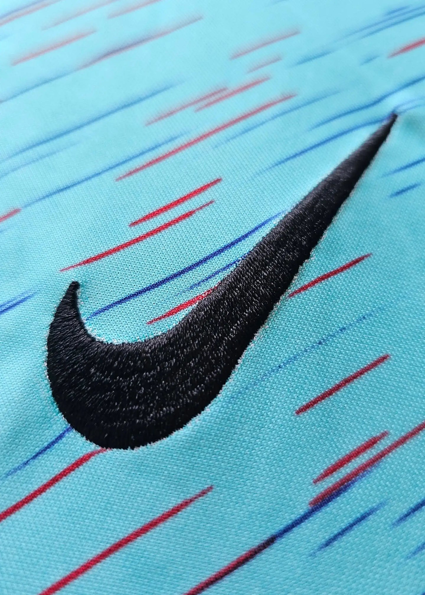 Close-up view of the black Nike swoosh logo against a blue and green patterned background.
