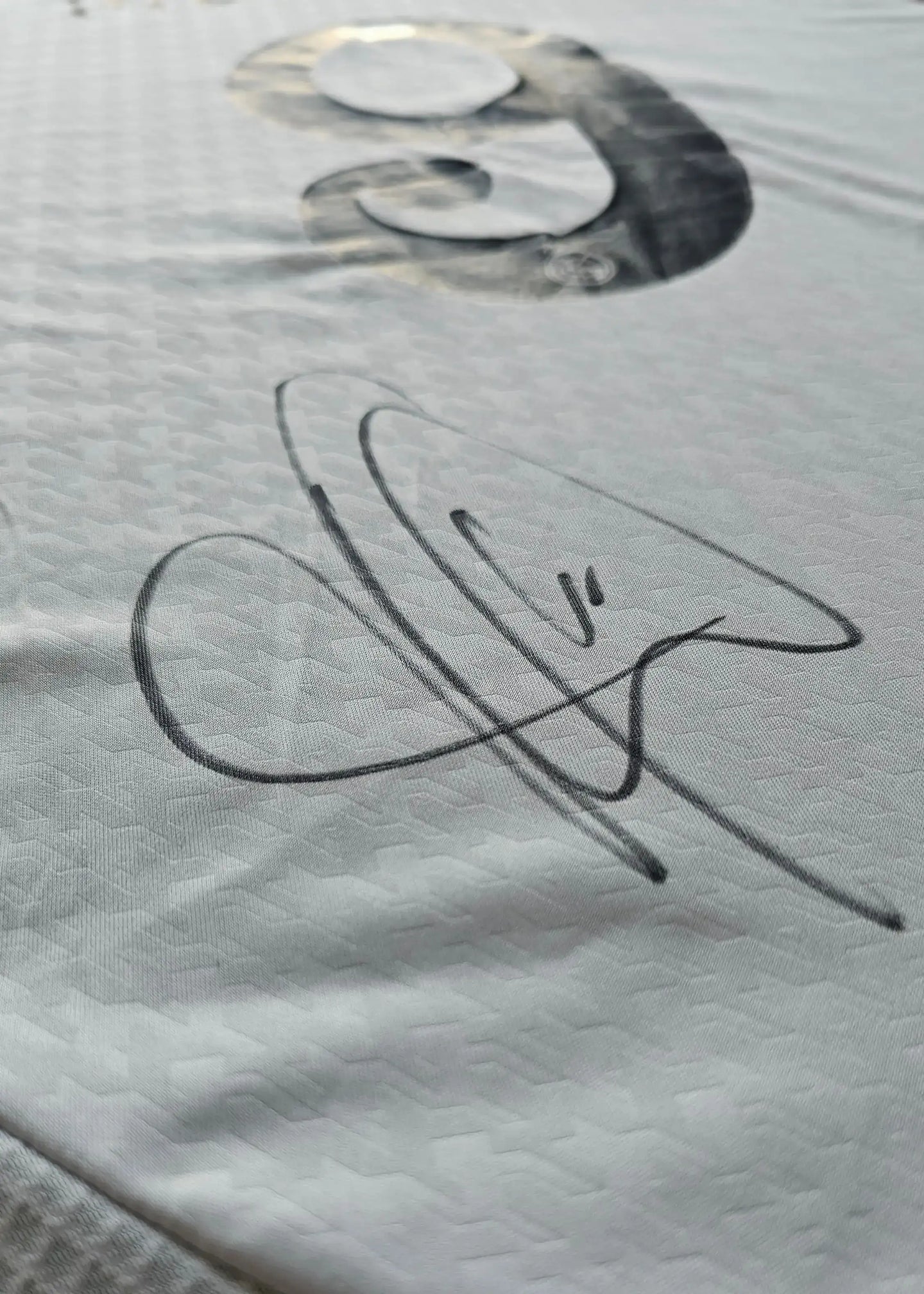 Signature detail of Kylian Mbappé on a white Real Madrid football shirt.
