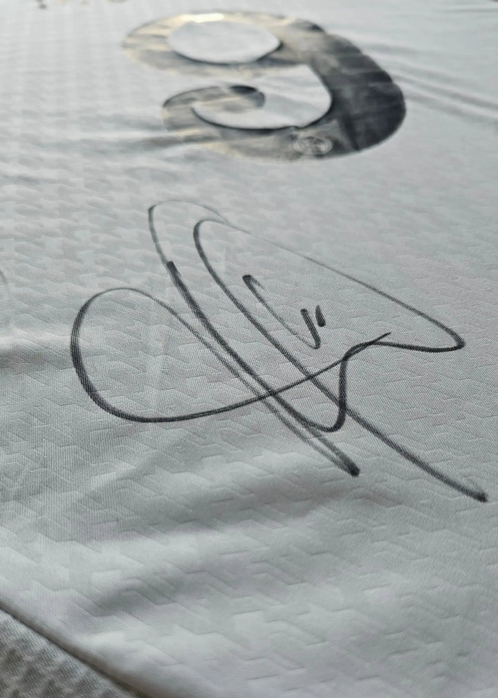 Close-up of the signature of Kylian Mbappé on a white football shirt.