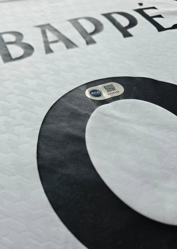 Detail of the name Mbappé and No. 9 on a signed white football shirt with authentication tag.