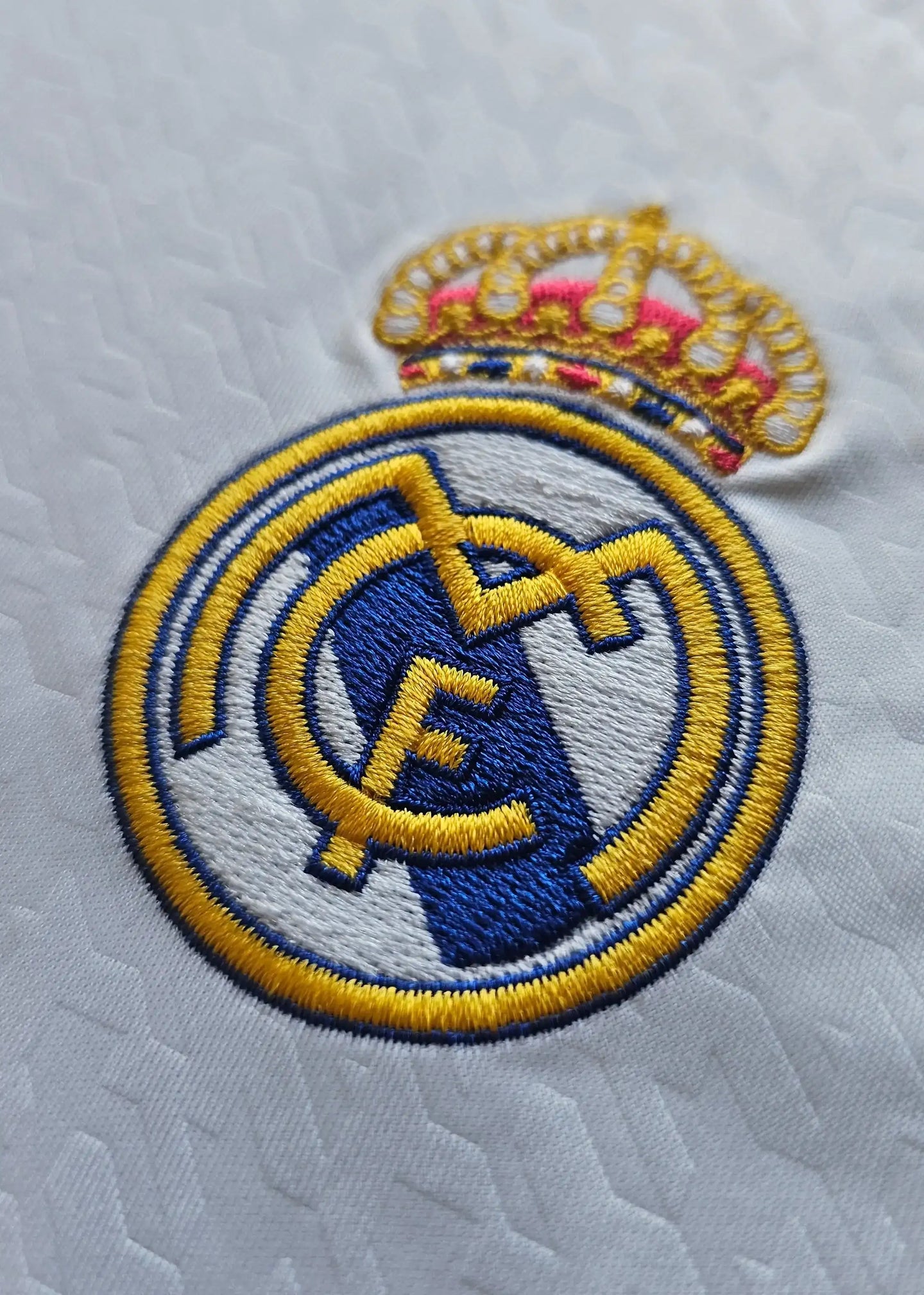 Real Madrid CF crest with golden crown and blue detail, prominently displayed on the shirt.