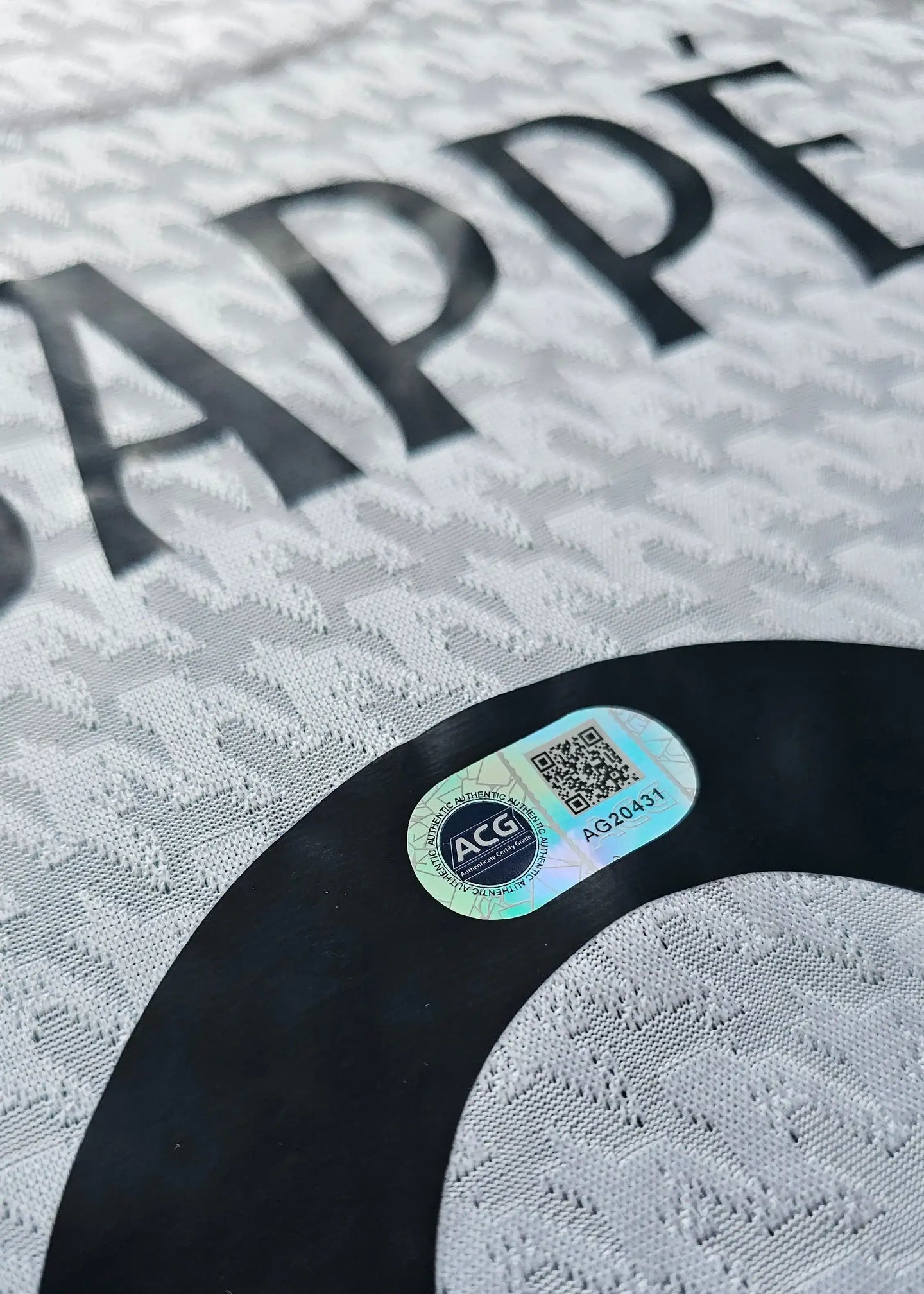 Kylian Mbappé name and No. 9 on a white football shirt with an authenticity tag below.