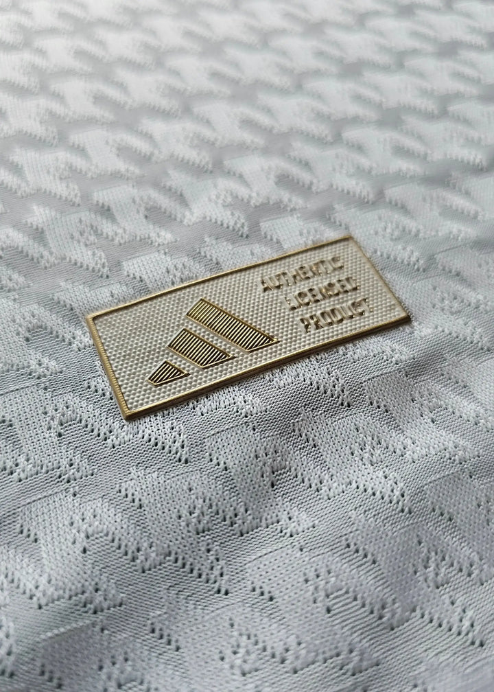 Close-up of the adidas authenticity tag on a white football shirt with textured details.